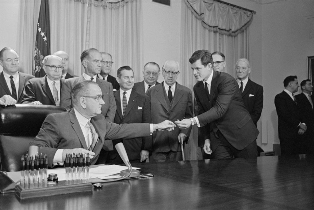 After signing a bill renaming the proposed National Cultural Center the John F. Kennedy Center for the Performing Arts here at the White House today, president Johnson hands one of the pens he used to senator Edward M. Kennedy. Photo courtesy Getty Images.