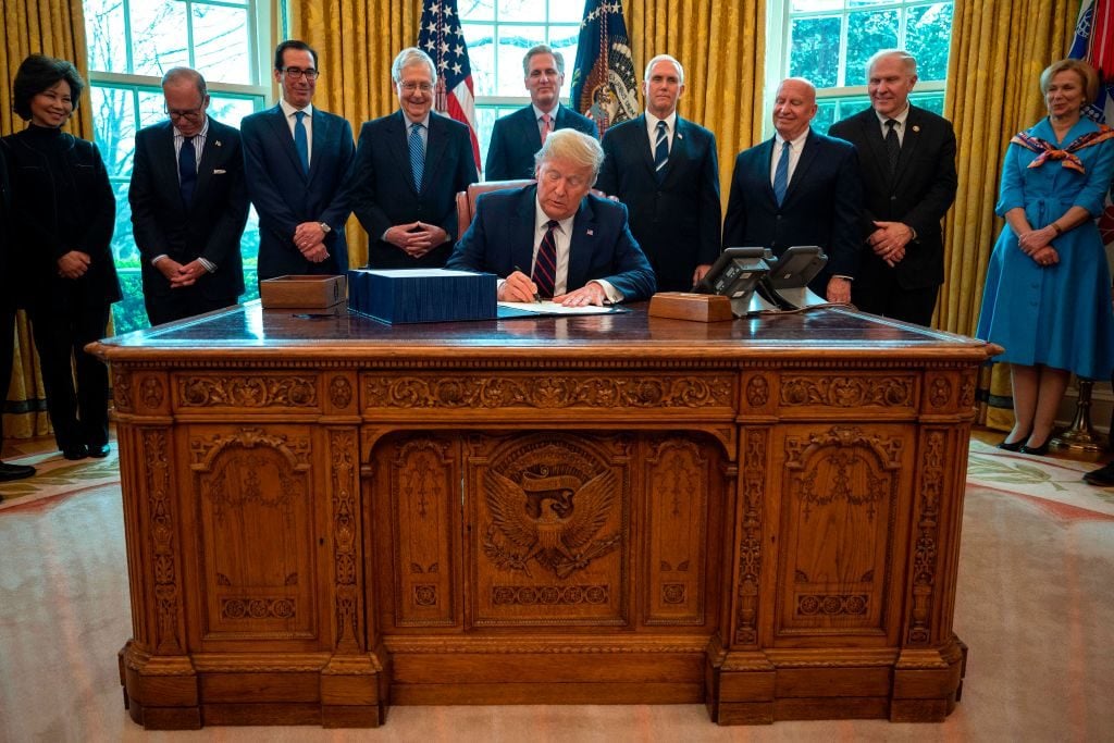 US President Donald Trump signs the CARES act, a $2 trillion rescue package to provide economic relief amid the coronavirus outbreak, at the Oval Office of the White House on March 27, 2020. Photo by Jim Watson/AFP via Getty Images.