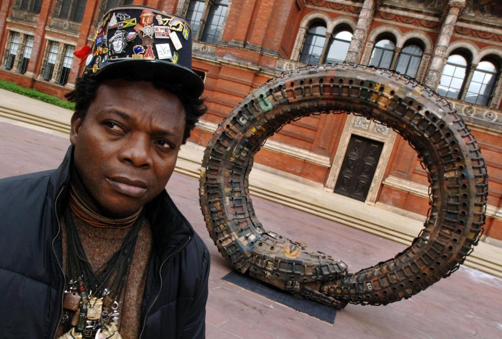 Beninese sculptor Romuald Hazoume with his work in the "Uncomfortable Truths - the shadow of slave trading on contemporary art and design" exhibition at London's V&A Museum. Photo by Fiona Hanson - PA Images/PA Images via Getty Images.