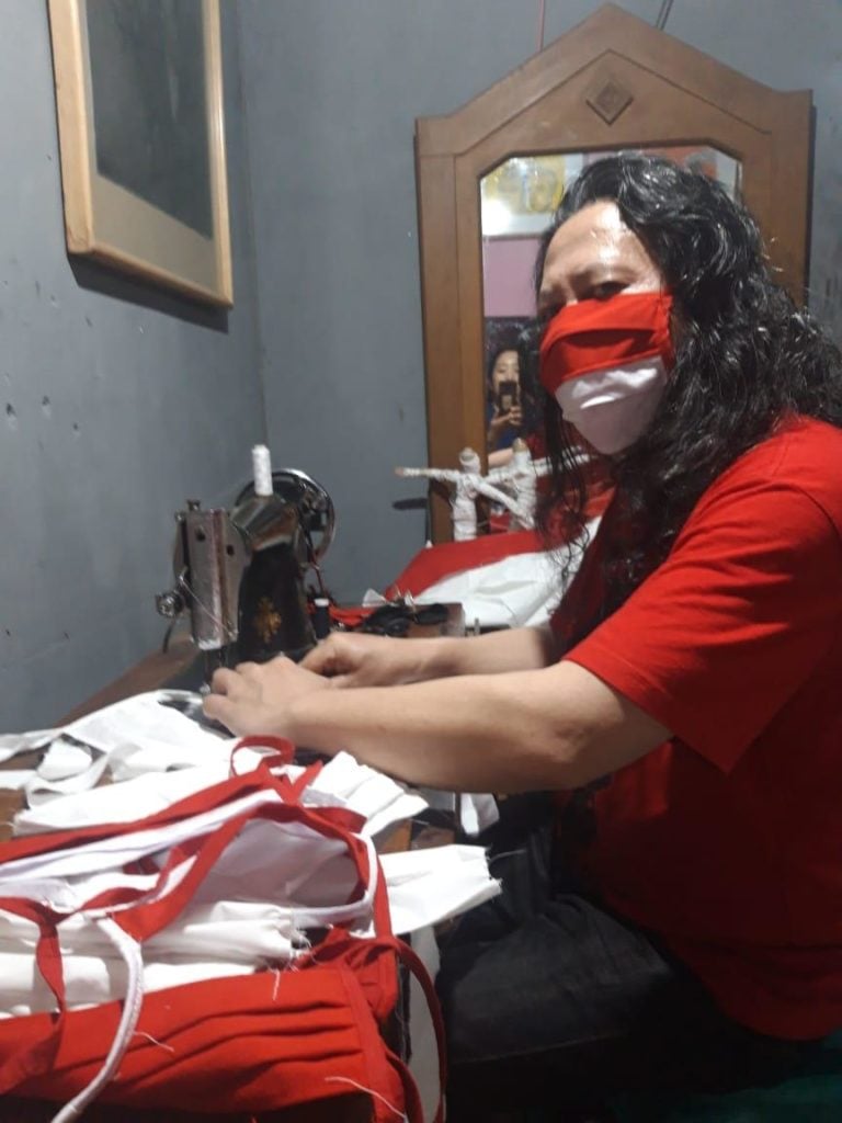 Isa Perkasa sews a red and white mask at his home in Bandung. Image courtesy the artist.