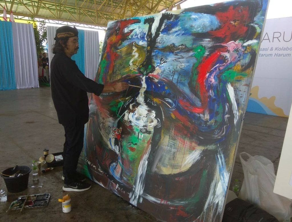 Tisna painting in the Citarum River revitalization project in 2019. Image courtesy the artist.