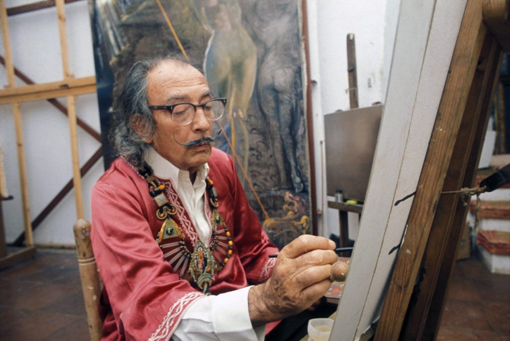 Salvador Dali painting in his studio in Spain, circa 1970. (Photo by Etienne Montes/Gamma-Rapho via Getty Images.