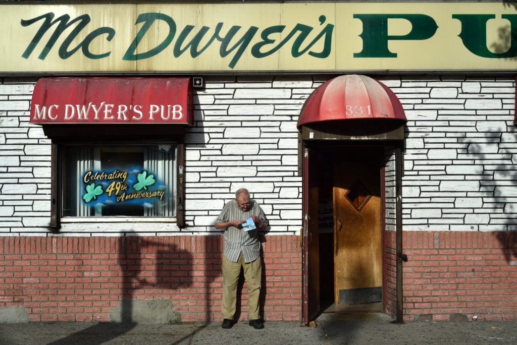 A patron fills in his Racing Form outside McDwyer’s, the last Irish pub in a Bronx neighborhood that used to host dozens. Norwood was once so heavily Irish that the sitting President of Ireland stopped through on one of her NYC visits; today, most of the Irish have moved to the suburbs or back to the “old Sod.” Since the photo was taken, McDwyer’s too has closed. Norwood 205 St, end of the D train; 2015. From the series "End of the Line." This is McDwyer's, the last Irish pub in the formerly Irish neighborhood. Photo courtesy of Taylor Chapman. 