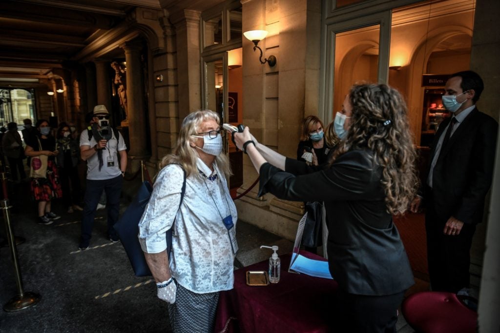 A staff member checks the body temperature of a visitor at the entrance of a Turner exhibition at the Jacquemart-Andre Museum in Paris on May 26, 2020. Photo by Stephane De Sakutin/AFP via Getty Images.