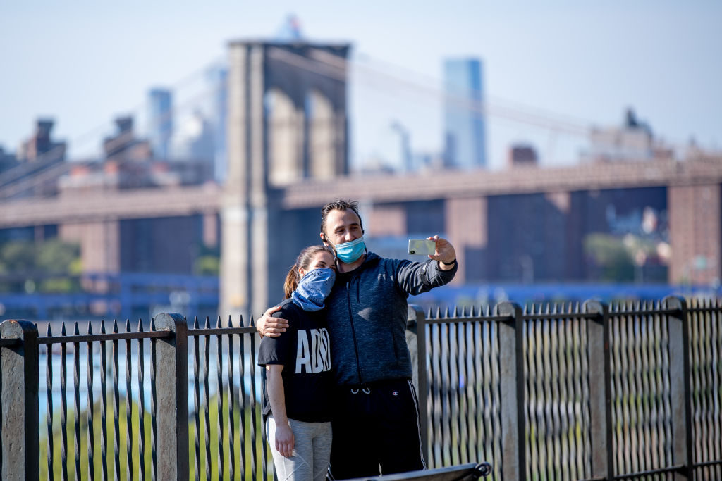 Visitors take a selfie and wear masks at the Brooklyn Heights Promenade with the Brooklyn Bridge in the background on May 10, 2020 in New York City. Photo by Roy Rochlin/Getty Images.