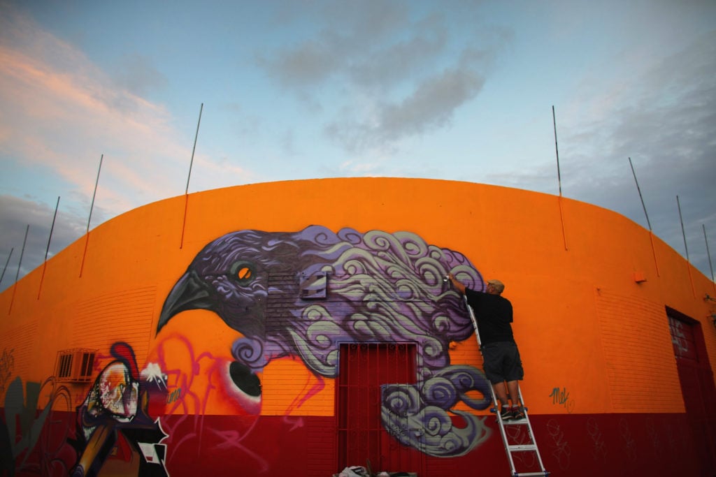 The artist known as Czrprz paints a raven on the wall of a building at park of Wynwood Walls (2012). Courtesy of Getty Images. Photo by Joe Raedle.