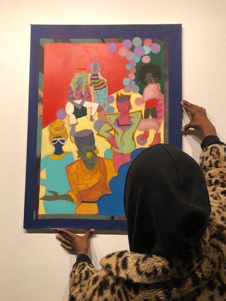 Curator John Wesley hanging <em>ART PROM</em>, a painting by AFRO SPK, at an art and fashion event in 2019. Photo by Yanina Sokolovska.