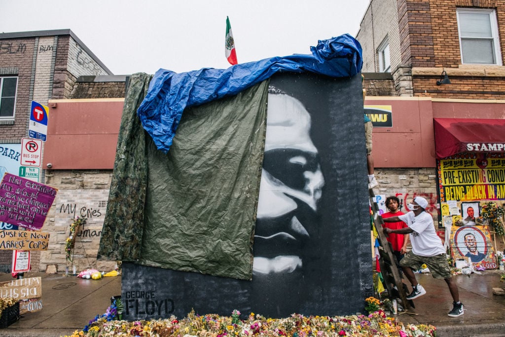 Men cover a painting of George Floyd at his memorial site on June 9, 2020 in Minneapolis, Minnesota. (Photo by Brandon Bell/Getty Images)