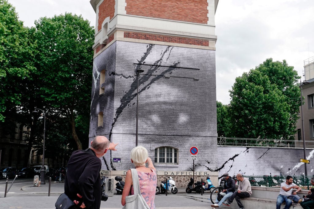 A Parisian couple looks at a mural in Paris mounted by students and street artist JR depicting the eyes of George Floyd and Adama Traore on June 10, 2020. (Photo by Daniel Pier/NurPhoto via Getty Images)