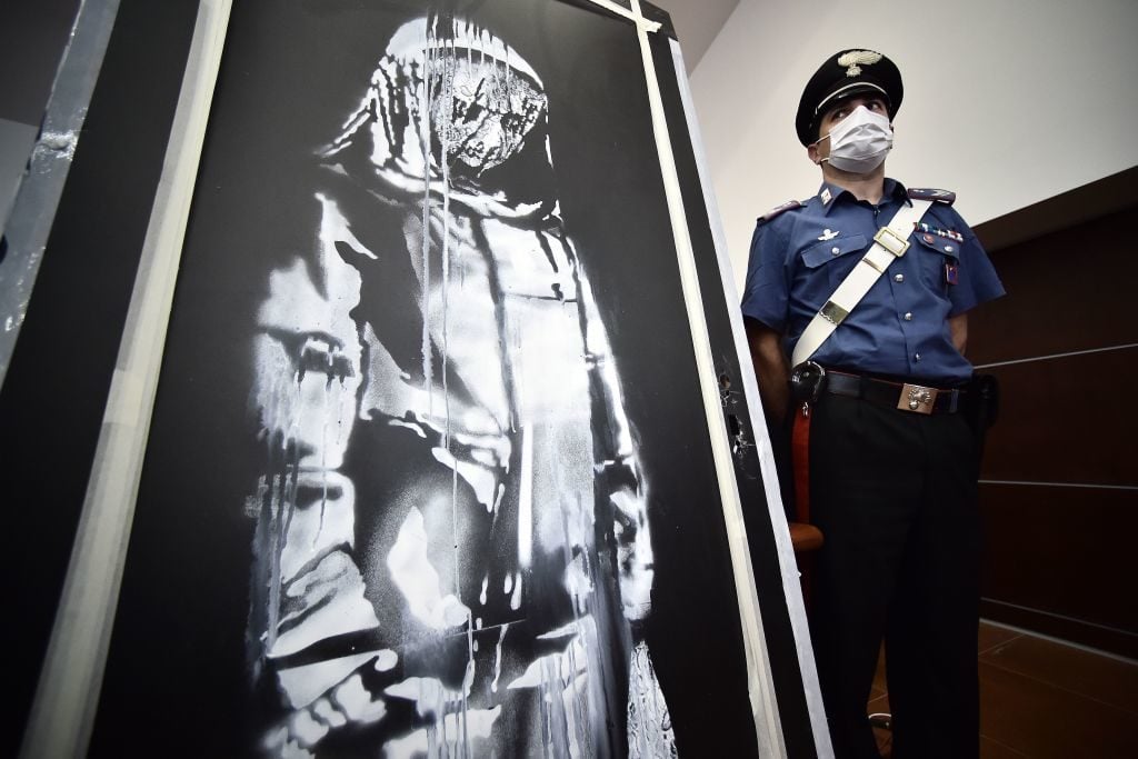 A policeman stands guard near a piece of art attributed to Banksy, that was stolen at the Bataclan in Paris in 2019, and found in Italy, ahead of a press conference in L'Aquila on June 11, 2020. Photo: Filippo Monteforte / AFP via Getty Images.