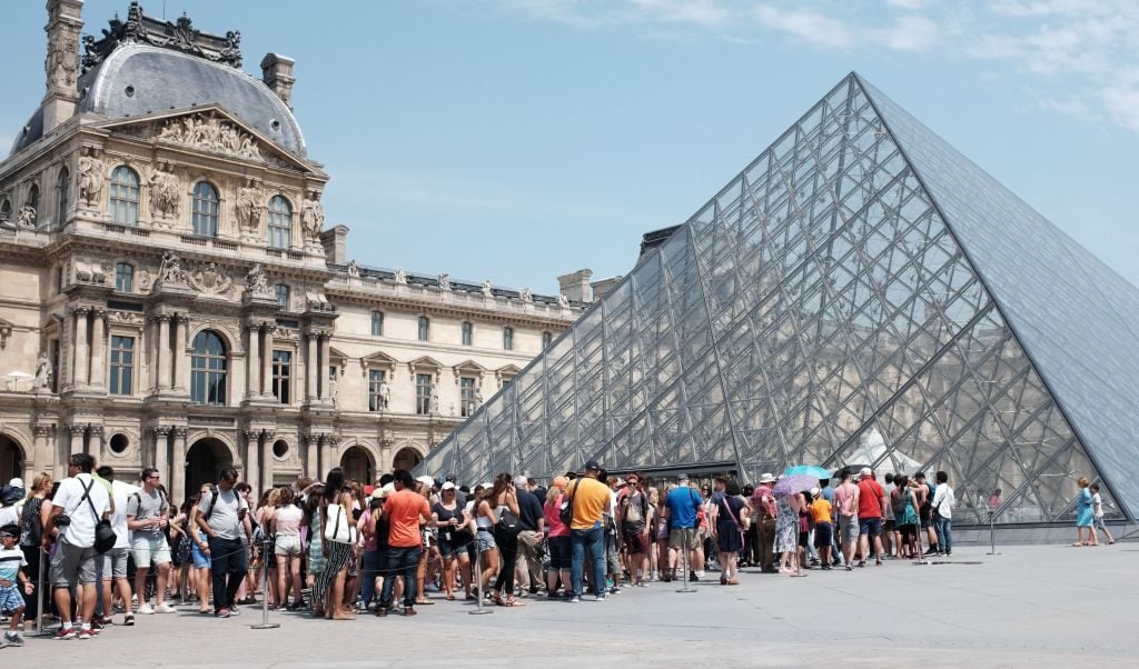 Tourists and visitors queue outside the Louvre Pyramid in Paris. Photo: Miguel Medina/AFP via Getty Images.