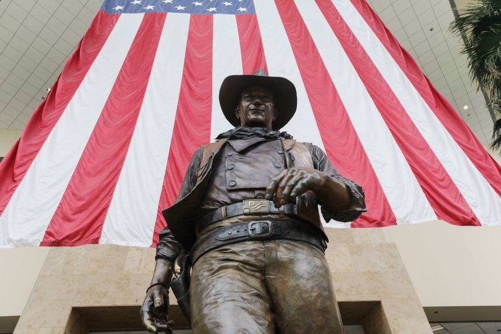 A statue of John Wayne is on display beneath an American flag in John Wayne Airport, located in Orange County, on June 28, 2020 in Santa Ana, California. Photo: Mario Tama/Getty Images.