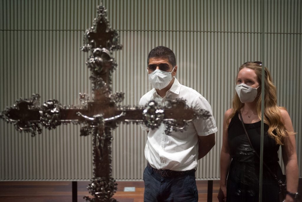 A couple wearing face masks are seen looking a religious cross, as part of the exhibition at Aduana Museum in Spain. (Photo by Jesus Merida/SOPA Images/LightRocket via Getty Images)