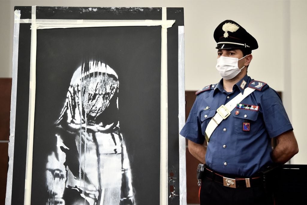An Italian Carabiniere poses near a piece of art attributed to Banksy, that was stolen at the Bataclan in Paris in 2019, and found in an abandoned farmhouse in Abruzzo. Photo by FILIPPO MONTEFORTE/AFP via Getty Images.