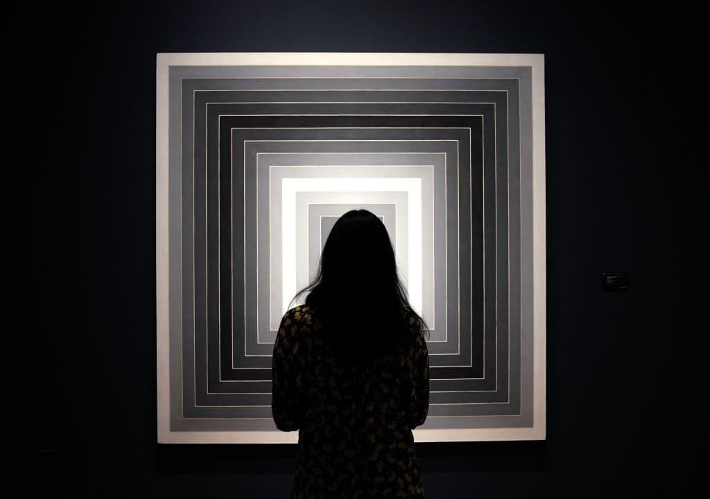 A woman looks at Frank Stella's "Sharpeville" during a press preview of Christie's relay-style "ONE" auction. Photo by Timothy A. Clary/AFP via Getty Images.