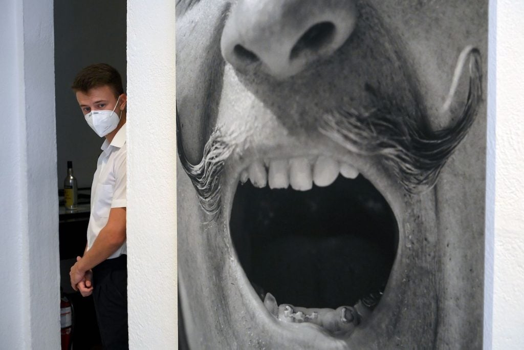 A man wearing a face mask stands next to a portrait of Spanish artist Salvador Dali on the reopening day of the Salvador Dali museum in Figueras, Spain. (Photo by Louis Gene/AFP, via Getty Images)