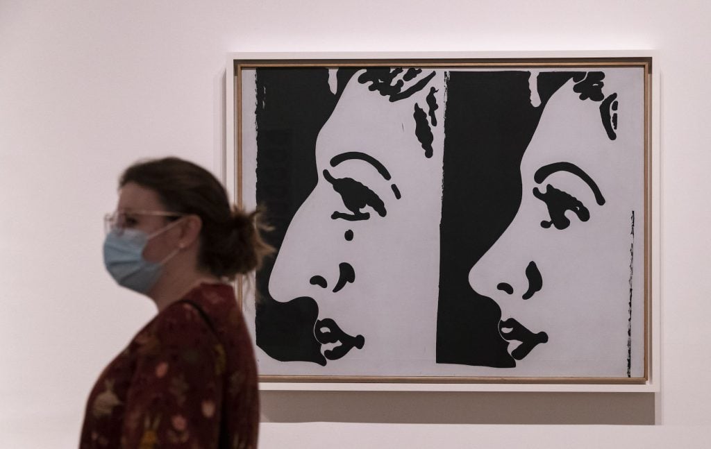 A visitor wearing a face mask walks by a piece of artwork by Andy Warhol during an exhibition at Tate Modern art gallery in London. (Photo by Han Yan/Xinhua via Getty)