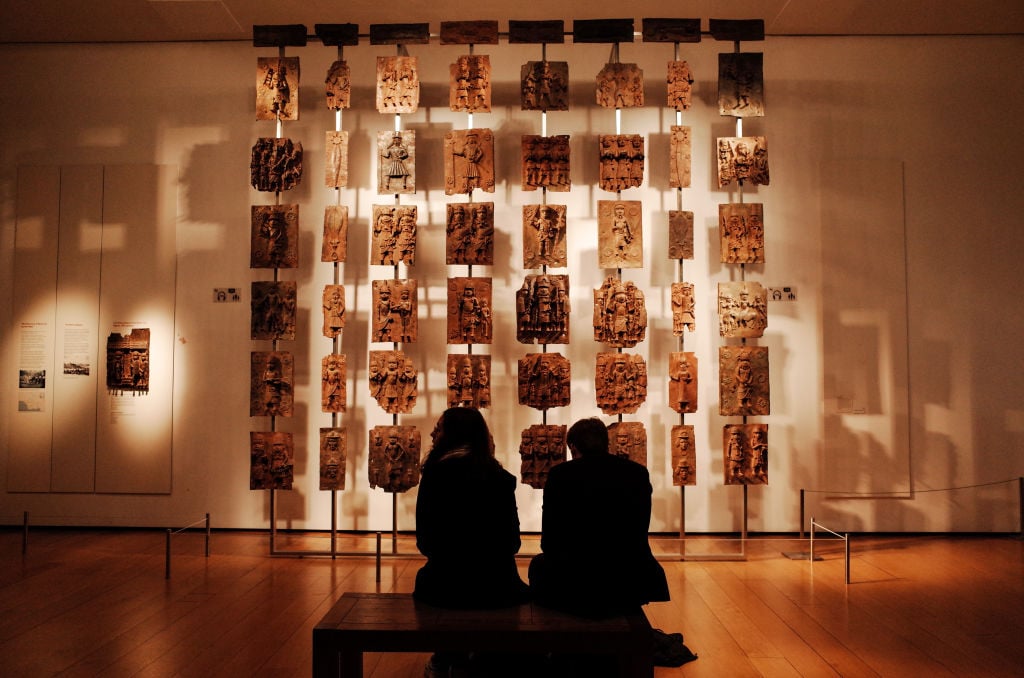 Visitors sit before the contentious Benin Bronzes at the British Museum in London. Photo by David Cliff/SOPA Images/LightRocket via Getty Images.