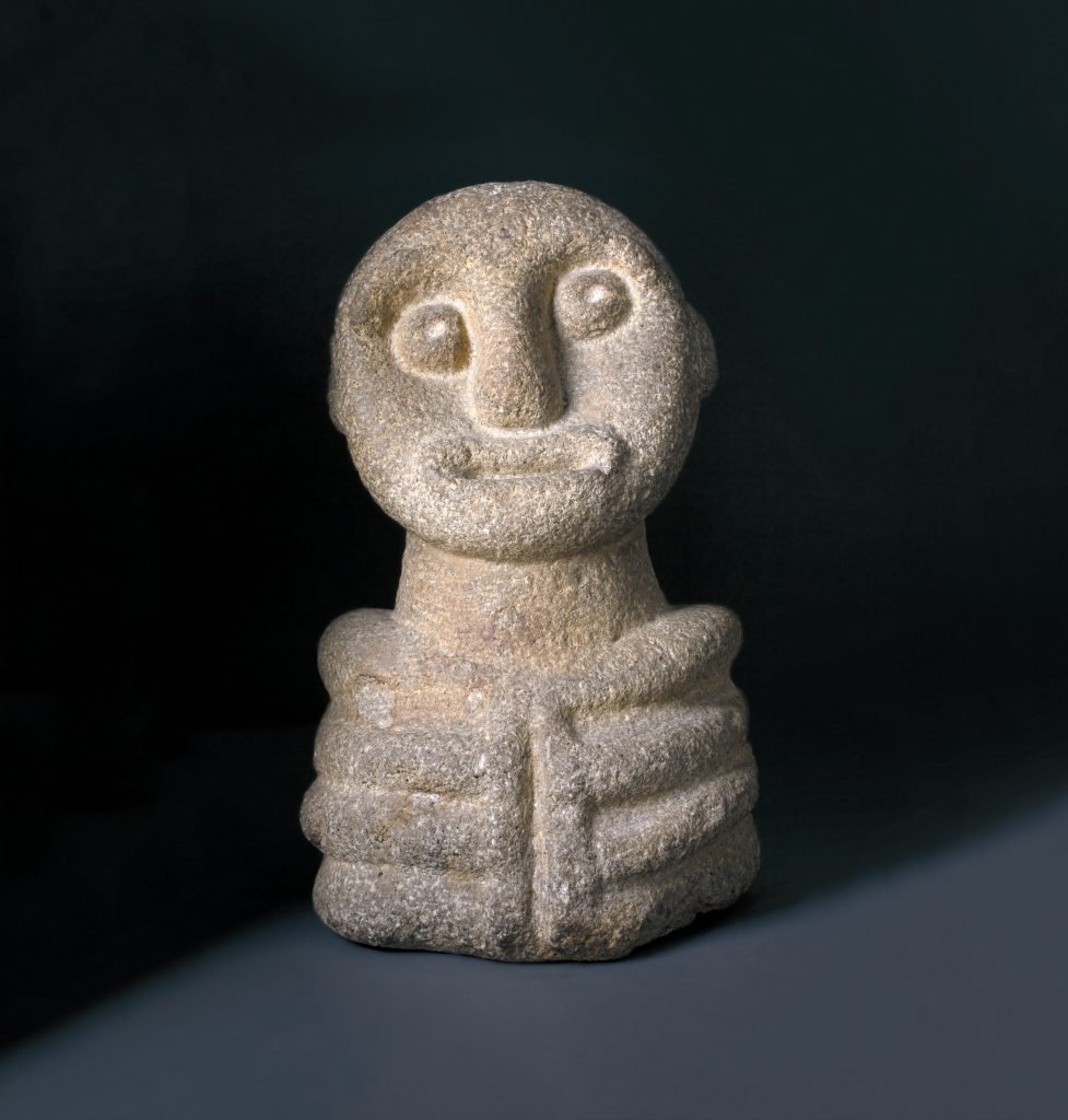 a stone sculpture of a small figure with a smiling face, against a black background