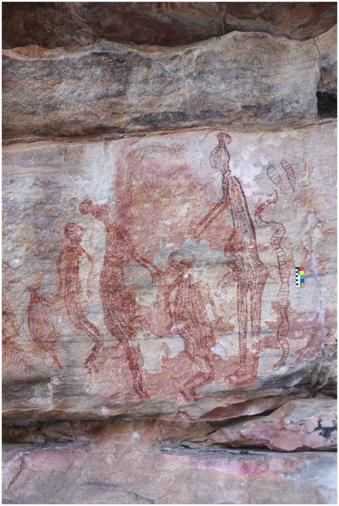 Scene of two male Maliwawas with ball headdresses reaching down to a shorter indeterminate human figure with a snake behind the male on the right and behind the left male a female and a macropod, Namunidjbuk. Photo by Paul Taçon.