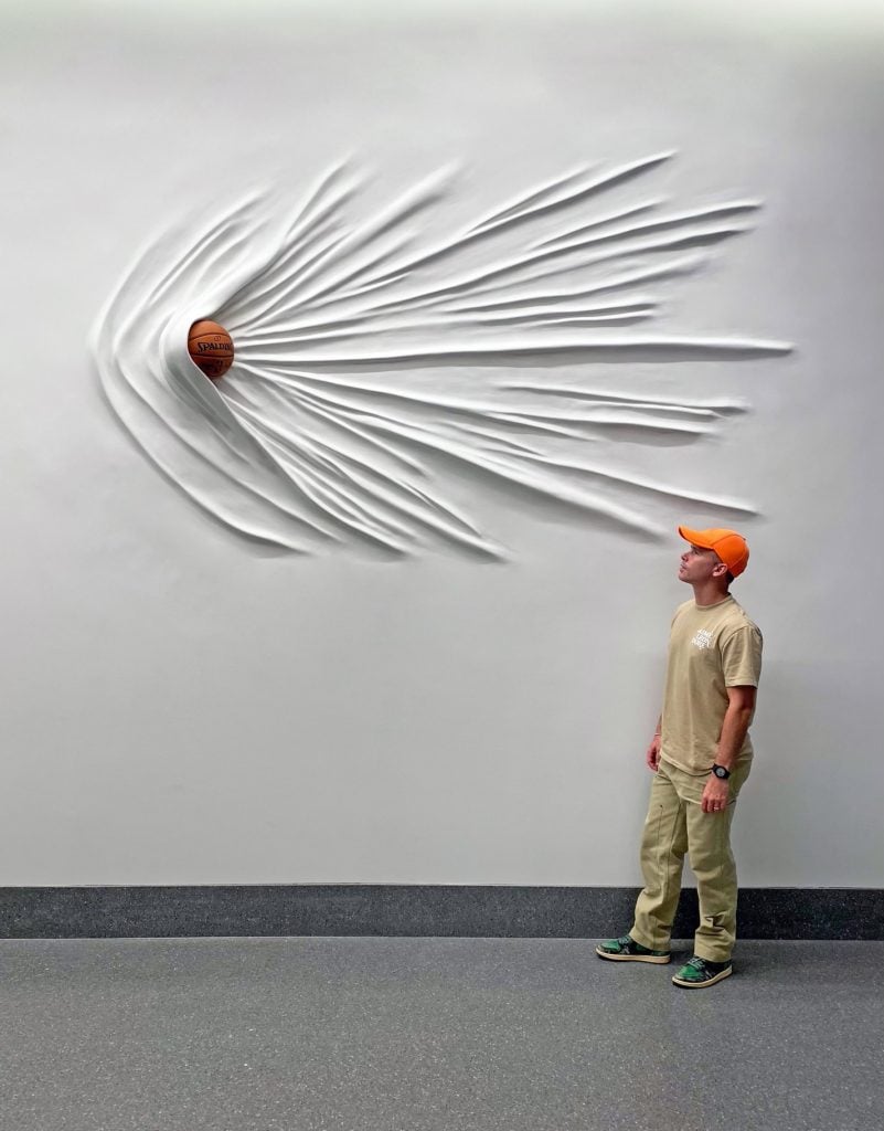Daniel Arsham with his site-specific installation <i>Moving Basketball</i> (2019), at Rocket Mortgage FieldHouse. Courtesy of the Cleveland Cavaliers.