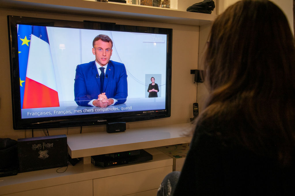 A member of the photographer’s family watches French President Emmanuel Macron on a television screen. Photo by Marc Piasecki/Getty Images.