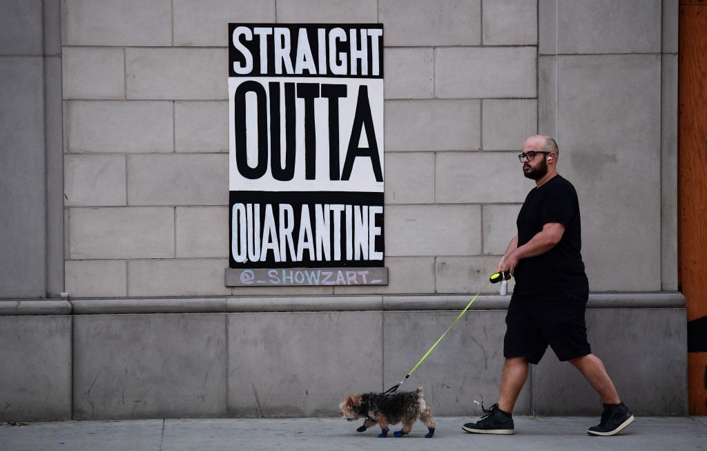 A man walks his dogs past a public art installation aimed at turning boarded up shopfronts into works of art in Los Angeles, California on April 28, 2020. The initiative was launched by street artist Jeremy Novy and Art Share LA, including work seen here by @_ShowzArt_. Photo by Frederic J. Brown/AFP, via Getty Images.