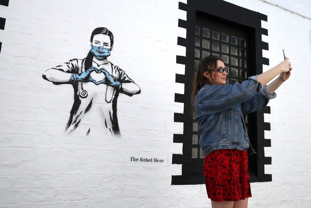 Hannah McGee takes a selfie beside a piece of art by the artist Rebel Bear after it appeared on a wall on Ashton Lane in Glasgow. Photo by Andrew Milligan/PA Images via Getty Images.