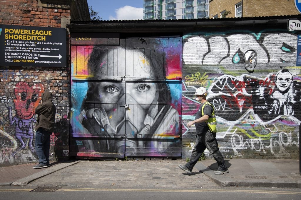 Virus face mask street art and graffiti on Brick Lane in Shoreditch as lockdown continues and people observe the stay at home message in the capital on May 12, 2020, in London. Photo by Mike Kemp/In PIctures via Getty Images.