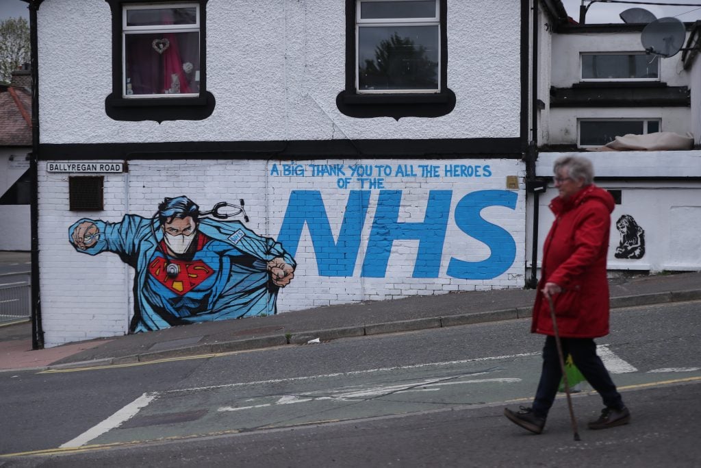 A woman walks past street art supporting the NHS, near to the Ulster Hospital in Dundonald, Belfast. Photo by Niall Carson/PA Images via Getty Images.