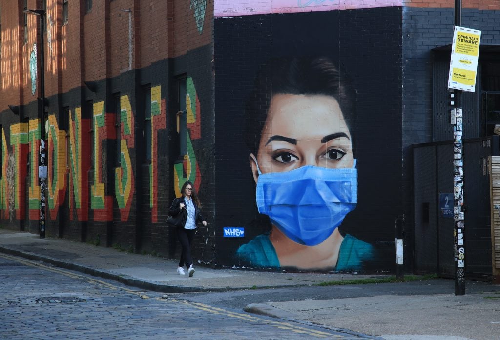 A woman walks past a piece of street art depicting an NHS worker on April 21, 2020 in the Shoreditch area of London, England. Photo by Andrew Redington/Getty Images.