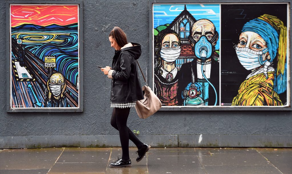 A pedestrian walks past MandiMixUps' coronavirus street art "Covid Collection," reimaginging historic artworks <em>The Scream</em>, <em>American Gothic</em>, and <em>Girl With a Pearl Earring</em> wearing masks, in Glasgow on September 2, 2020 after the Scottish government imposed fresh restrictions on the city after an rise in cases of the novel coronavirus. Photo by Andy Buchanan/AFP via Getty Images.