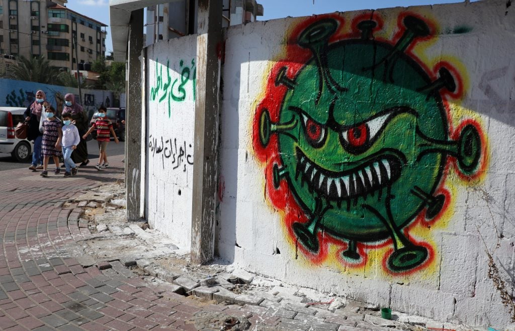 Palestinians, wearing protective face masks,walk past street art showing a COVID-19 virus, in Gaza city on October 5, 2020. Photo by Majdi Fathi/NurPhoto via Getty Images.