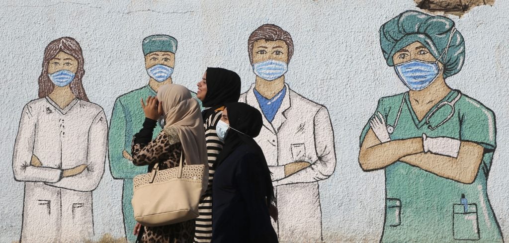 Palestinian women walk past street art showing doctors mask-clad due to the COVID-19 coronavirus pandemic, in Khan Yunis in the southern Gaza Strip, on November 12, 2020. Photo by Mohammed Abed/AFP via Getty Images.