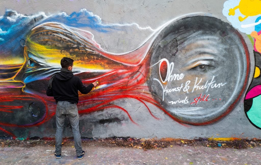 Berlin artist S. G. Raum works on a mural featuring the words: "Without art and culture it gets quiet..." on a segment of the Berlin wall in Berlin's Mauerpark on November 15, 2020. Photo by John MacDougall/AFP via Getty Images.