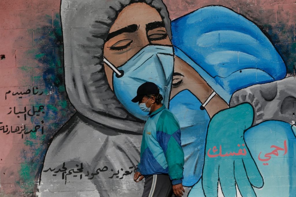 A Palestinian man walks past street art showing doctors mask-clad due to the COVID-19 coronavirus pandemic in the Nusseirat refugee camp in the central Gaza Strip on November 16, 2020. Photo by Mohammed Abed/AFP via Getty Images.
