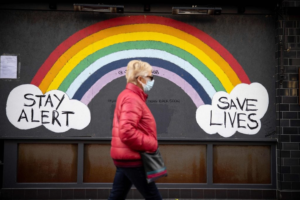 A pedestrian wearing a face mask or covering due to the COVID-19 pandemic, walks past COVID-19 street art, advising to "Stay Alert" and "Save Lives" in central London, on November 22, 2020. Photo by Tolga Akmen/AFP via Getty Images.
