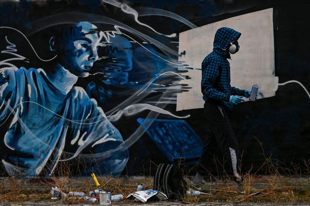 Street artist SF paints a mural on a wall in Athens, inspired by the second lockdown in Greece due to the COVID-19 pandemic, in Athens on November 25, 2020. Photo by ARIS MESSINIS/AFP via Getty Images.