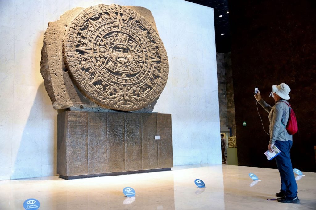 A visitor taking a photograph of the Stone of the Sun or Aztec Calendar as it is also known during a reopening ceremony at Museo Nacional de Antropologia on November 11, 2020 in Mexico City, Mexico. Photo by Clasos/Getty Images.