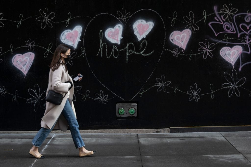 A woman wearing a mask walks past street art of hearts that reads, "Hope" on December 10, 2020 in New York City. Photo by Alexi Rosenfeld/Getty Images.