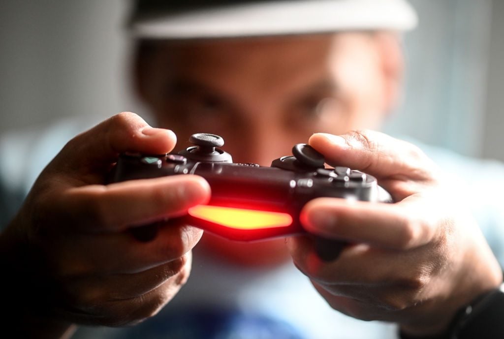 A young man plays in front of the television with the Playstation game console. Photo by Britta Pedersen/picture alliance via Getty Images.