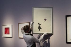 A staff member holds up Banksy's Girl with Balloon at Christie's. Photo by Wiktor Szymanowicz/Barcroft Media via Getty Images.
