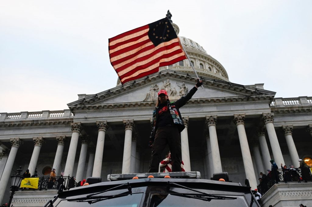 A Trump supporter waves a flag as he stands on a government vehicle in front of the US Capitol on January 6, 2021. (Photo by Andrew Caballero-Reynolds/AFP/Getty Images.