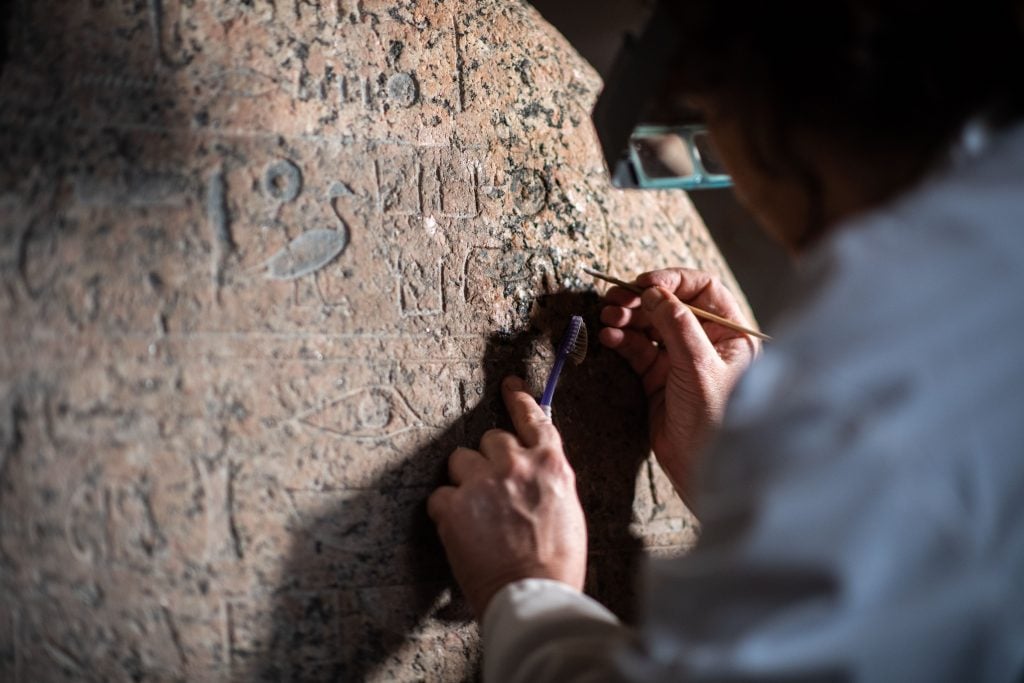 Sophie Duberson, of the restoration department of the Louvre Museum cleans the Egyptian funerary stele Senusret. Photo by MARTIN BUREAU/AFP via Getty Images.