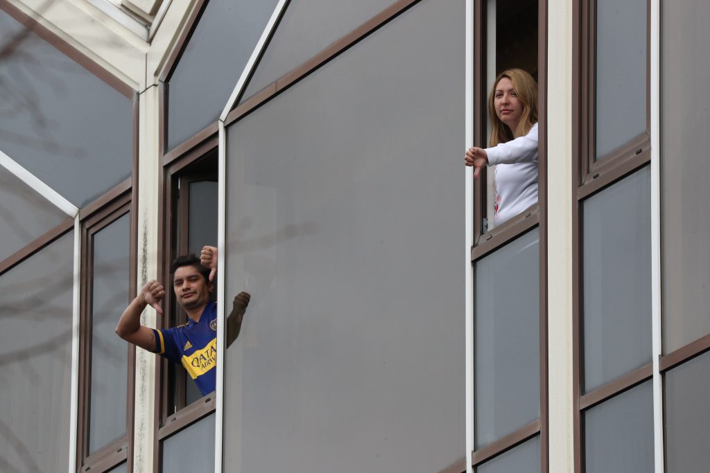 Two quarantined travellers in the same room making a thumbs down gesture out of their windows in the Radisson in London in February 2021. Photo by Jonathan Brady/PA Images via Getty Images.