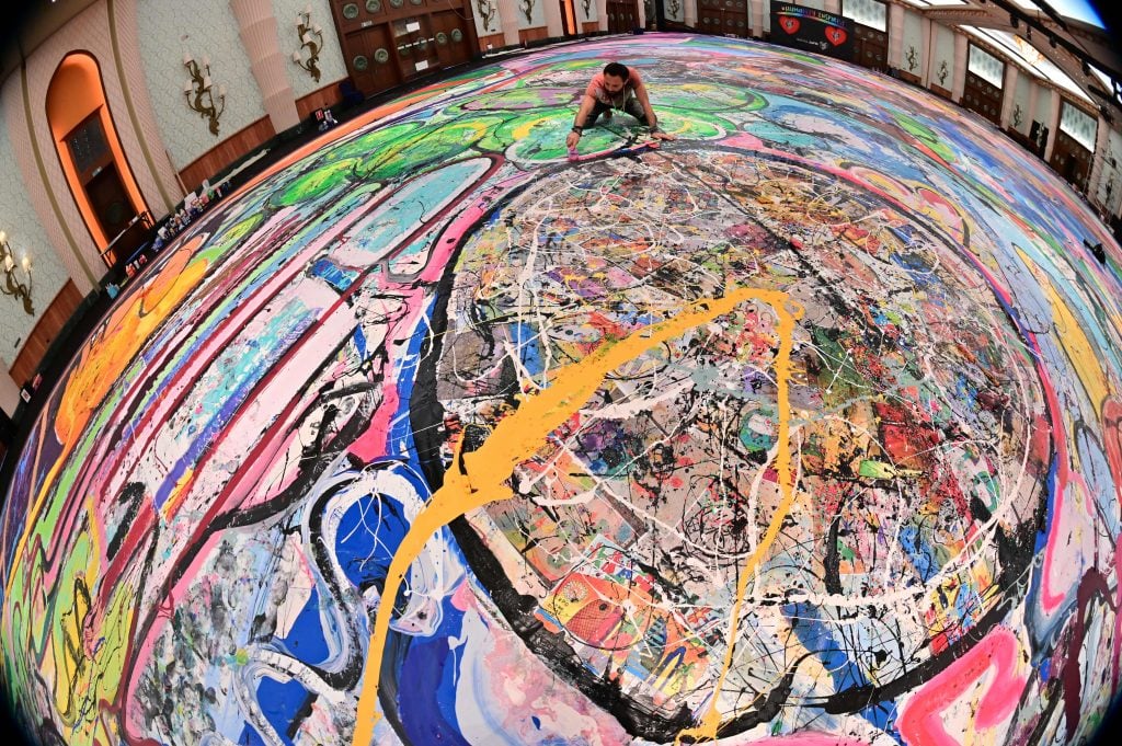 A picture taken with fisheye lens shows contemporary British artist Sacha Jafri working on his record-breaking painting entitled <em>The Journey of Humanity</em> on September 23, 2020, in the Emirati city of Dubai. Jafri spent months of lockdown at the Atlantic, the Palm, hotel due to the pandemic. The painting's $62 million sale will fund health and education initiatives for children living in poverty worldwide. Photo by Giuseppe Cacace/AFP via Getty Images.
