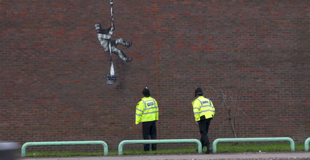 Two police officers investigate the newly painted mural. Screenshot courtesy of the artist.