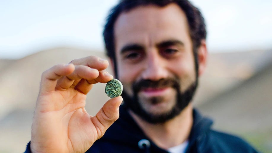Archaeologist Hagay Hamer holding a Bar Kokhba coin found in the desert. Photo by Yoli Schwartz, courtesy of the Israel Antiquities Authority.