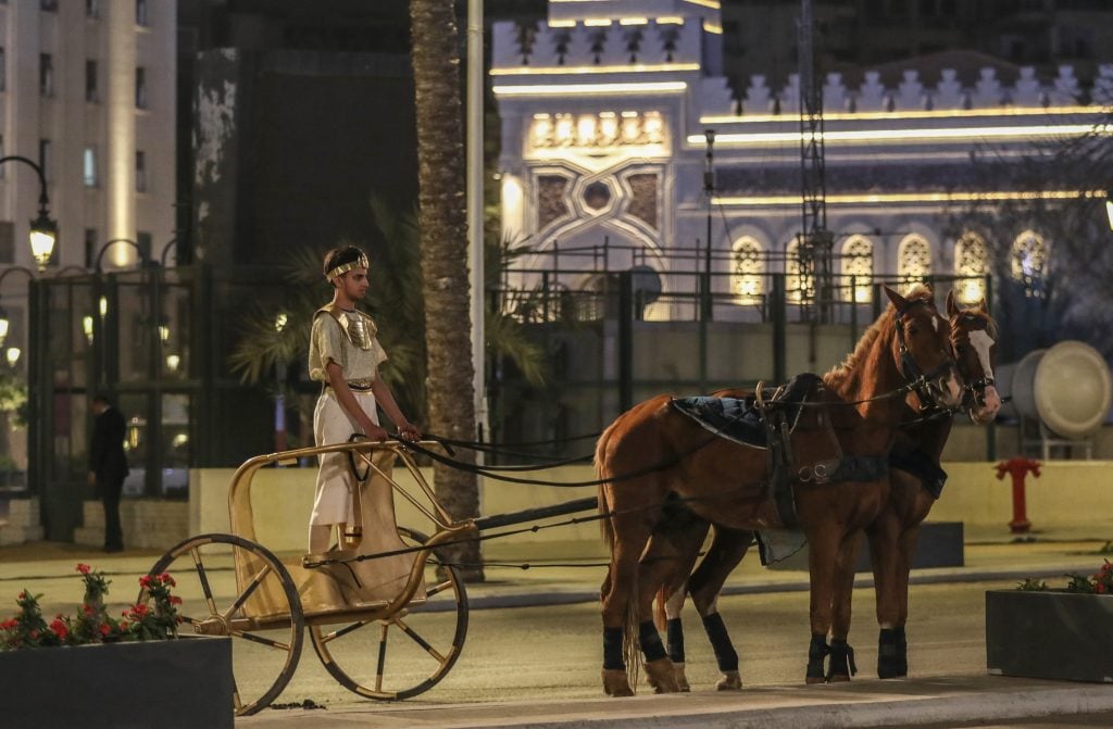 An artist in old traditional costume rides a horse-drawn carriage as specially designed vehicles transport 22 mummies in a convoy from the Egyptian Museum in Tahrir Square to the new National Museum of Egyptian Civilization, during the Pharaohs' Golden Parade in Cairo, Egypt on April 03, 2021. Photo by Stringer/Anadolu Agency via Getty Images.