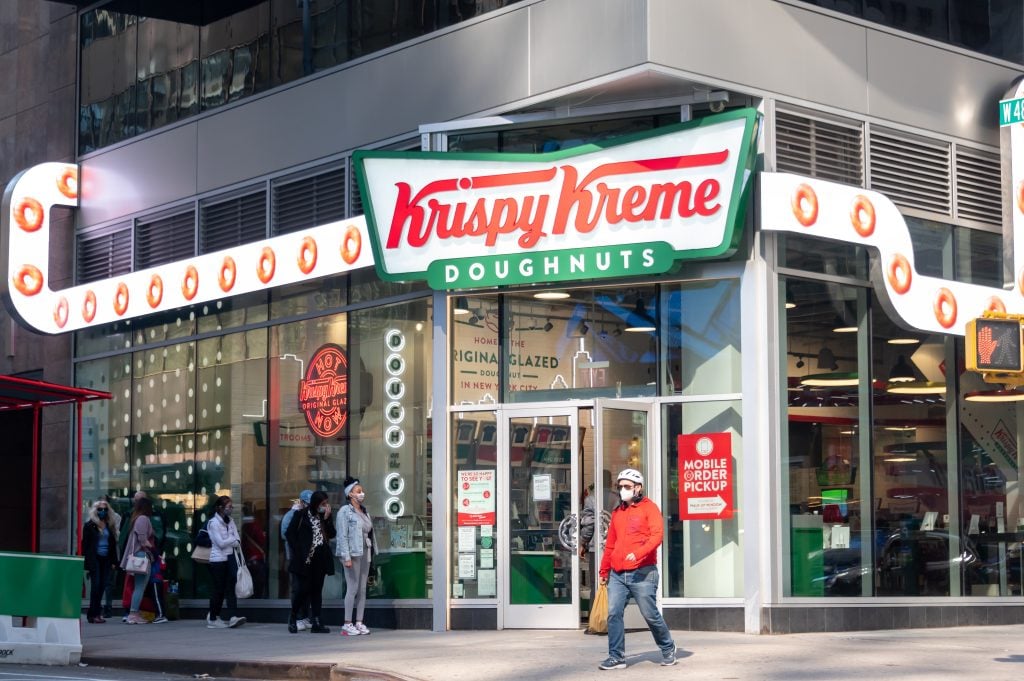Customers line up outside Krispy Kreme in Times Square days after the mega-bakery began offering a free glazed donut per day to anyone with proof of vaccination, sparking a controversy we in the art world are unlikely to replicate on multiple levels. (Photo by Noam Galai/Getty Images)